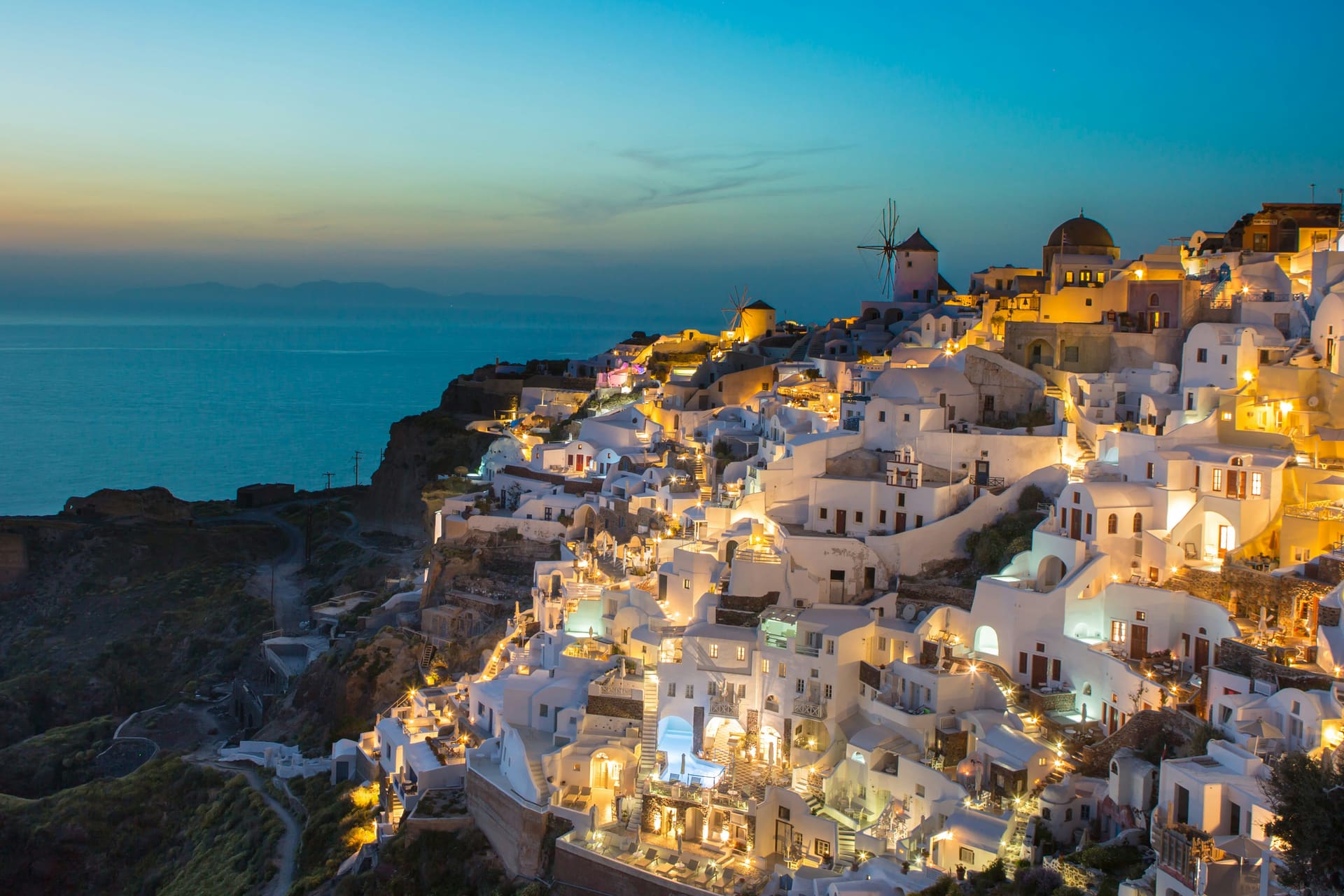 Whitewashed Oia lit up at dusk on the Santorini cliffs above the Aegean