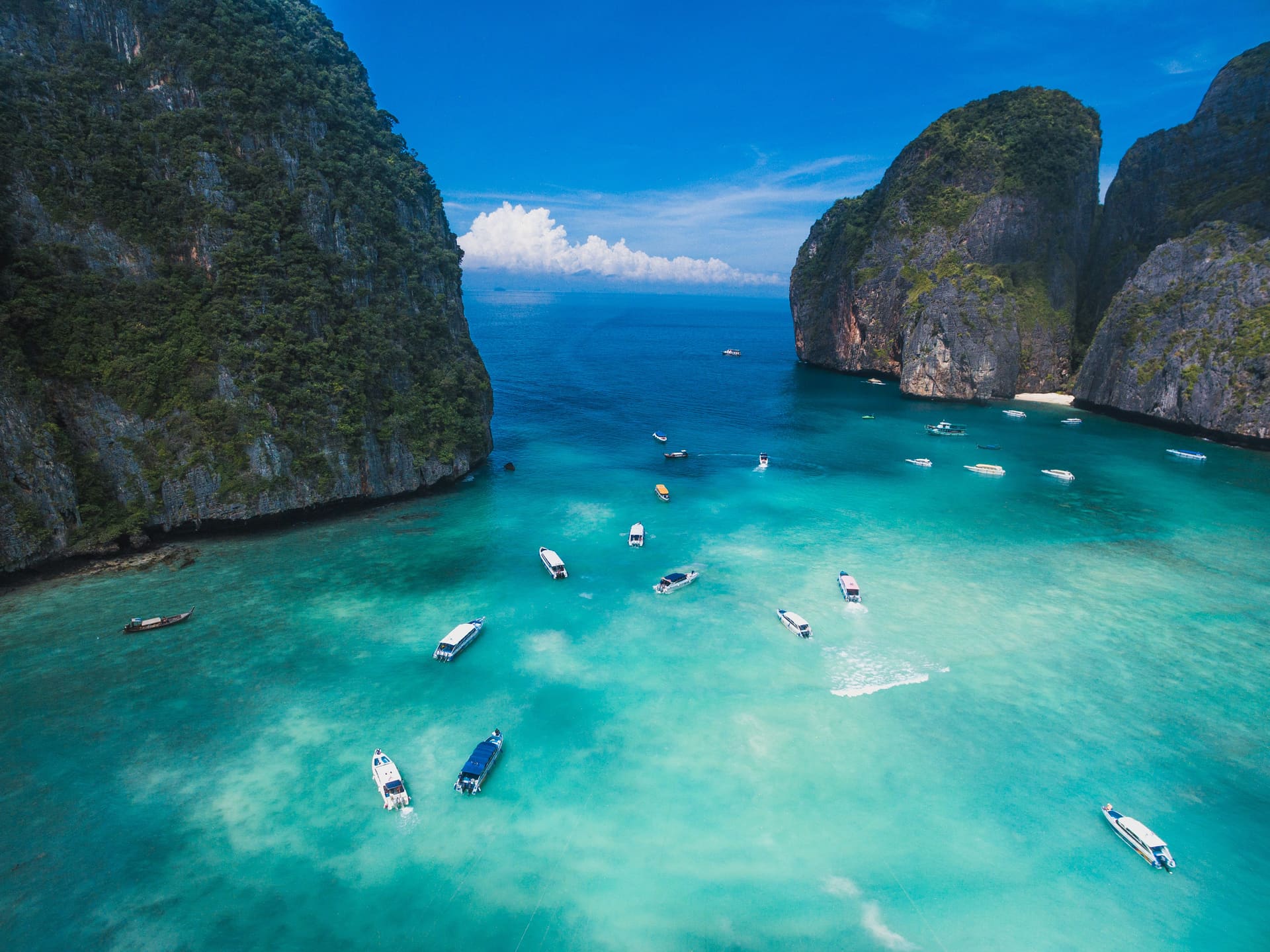 A turquoise bay ringed by limestone cliffs with boats at anchor in Thailand